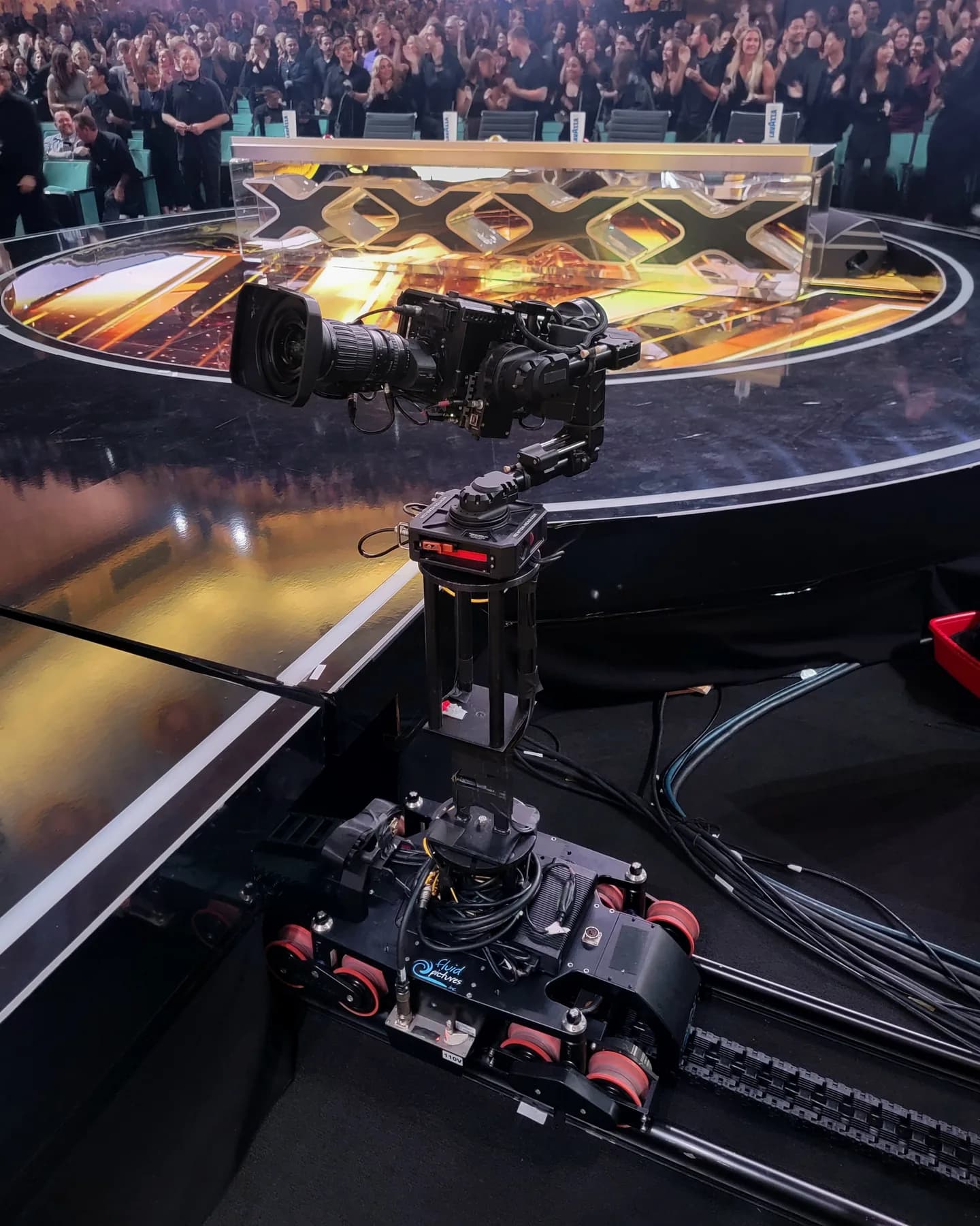 Broadcast camera on a shop-built riser mounted to a dolly, running on track at the edge of a stage