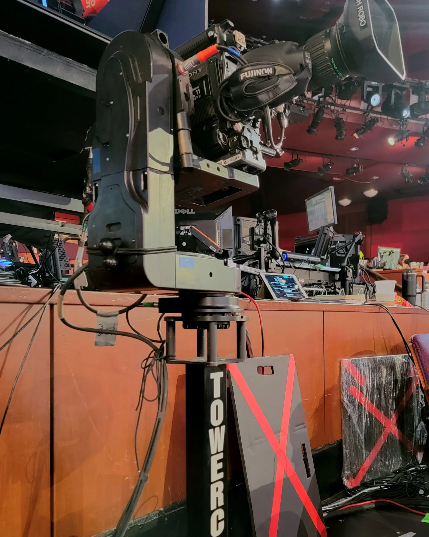 Towercam Mini with a broadcast camera set against a set desk, the TOWERCAM name running down its column