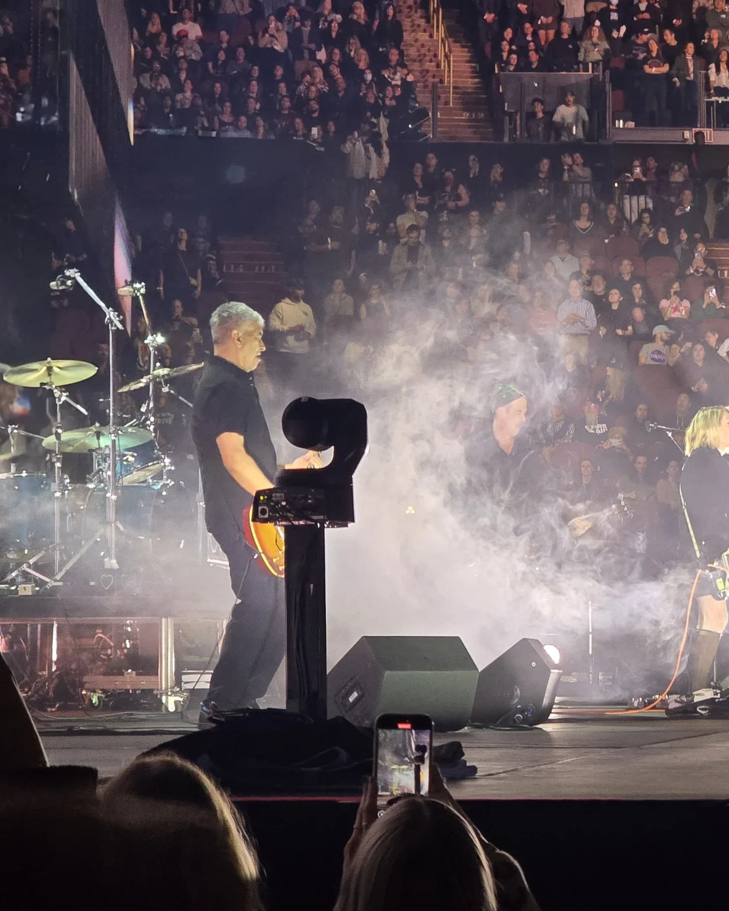 Towercam Mini carrying a robotic camera on stage beside a live band, with haze and the crowd in front