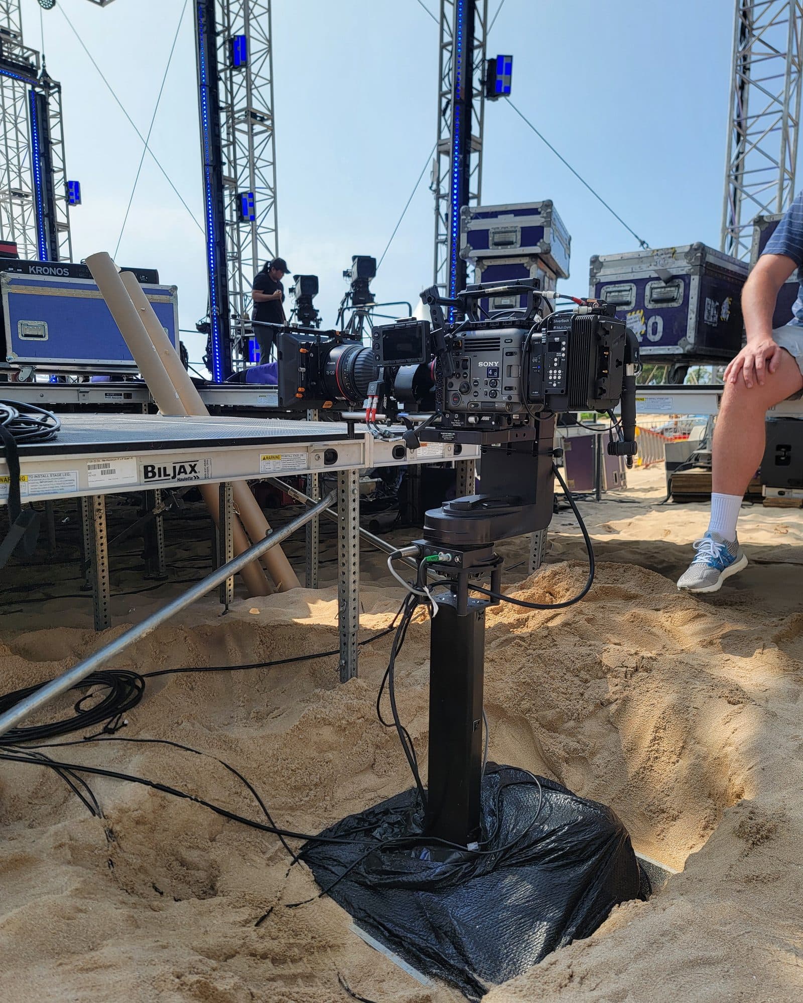 Towercam Mini planted in sand beside an outdoor stage, carrying a broadcast camera